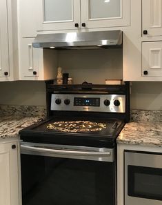 a stove top oven sitting inside of a kitchen next to white cupboards and drawers