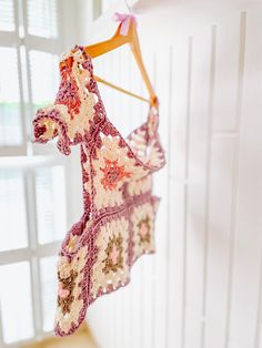 a crocheted piece of clothing hanging from a clothes hanger in front of a window