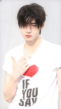 a young man with black hair holding a red heart in his right hand and wearing a white t - shirt that says if you say