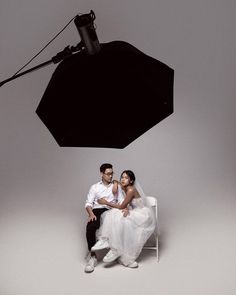 two people sitting on a chair in front of a black and white background with an umbrella