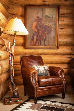 a chair and lamp in front of a log wall with a cowboy painting on it