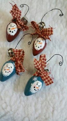 four ornaments with snowmen on them are sitting on a white blanket and one has a red bow