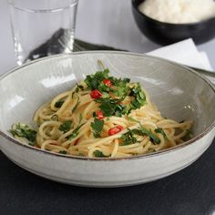 a white bowl filled with pasta and garnished with parsley next to a glass of water