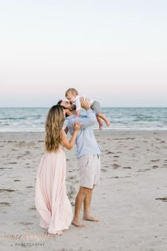 a family playing on the beach in front of the ocean at sunset with their toddler