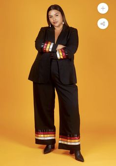 a woman standing with her arms crossed in front of an orange background wearing black pants and a blazer