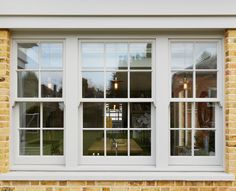 a brick building with three windows and white trim on the outside, one window is open to let in light