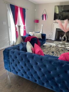 a living room with blue velvet couches and pink pillows on the back of them