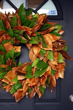 a wreath is hanging on the front door with green and brown leaves around it's edges