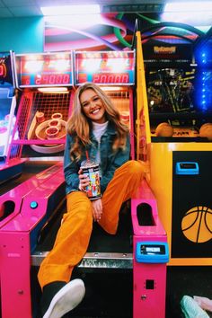 a woman sitting on top of a pink and yellow machine with basketball hoops in the background