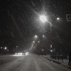 a snowy street at night with cars driving on it and people walking in the snow