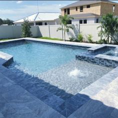 an outdoor swimming pool in a backyard with stone pavers and water feature, surrounded by greenery