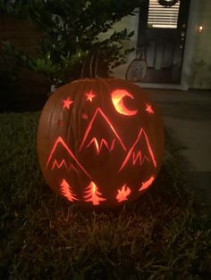 a carved pumpkin sitting in the grass with mountains and stars on it's face