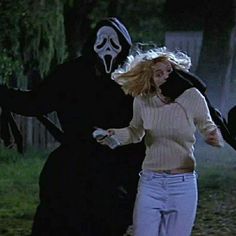 two people dressed in costumes running through the grass with one person wearing a ghost mask