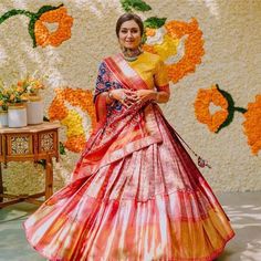 a woman in an orange and yellow sari standing next to a wall with flowers on it