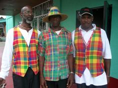 three men standing next to each other in front of a green building wearing colorful vests and hats