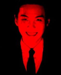 a man in a suit and tie smiling at the camera with red light shining on him