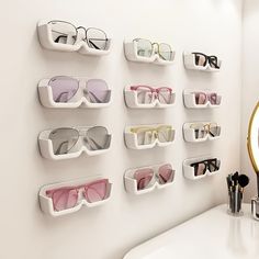 several pairs of sunglasses are hanging on the wall next to a mirror and makeup brush