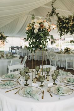 A gold floral vessel, a pink, peach and white arrangement sits at the top, below is gold trimmed plates and green goblets with matching gold silverware. Emerald Green And Gold Wedding Ideas, Blush Sage And Gold Wedding Decor, Sage Gold Wedding, Green Wedding Theme Receptions, Olive Green Wedding Decorations, Olive Green Reception Decor, Emerald Green Wedding Place Settings, Olive Green Gold Wedding, Sage Green And Gold Wedding Table Decor