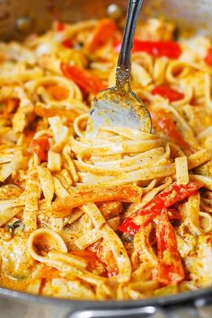 a fork is stuck into some pasta with sauce and peppers on it in a skillet