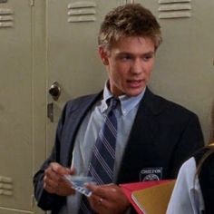 a man in a suit and tie standing next to a woman with folders on her lap