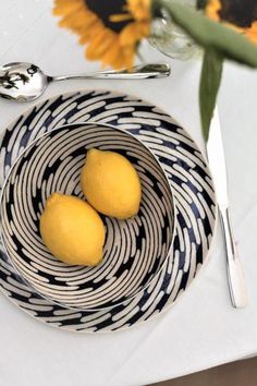 two lemons sit in a bowl on a table next to a fork and knife