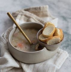 a bowl filled with soup and crackers on top of a white cloth next to a wooden spoon