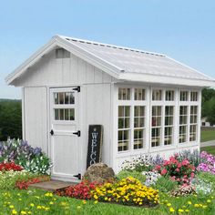 a small white shed with flowers around it