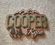 a wooden sign that says cooper ryan on the side of a building with mountains in the background