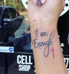 a woman's wrist tattoo with the words i am enough and a cross on it