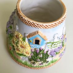 a vase with flowers painted on it and a birdhouse in the center, sitting on a table