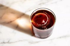 a glass filled with liquid sitting on top of a white marble countertop next to a light