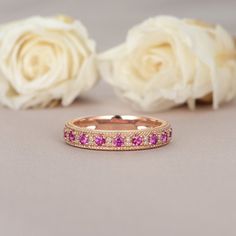 a close up of a wedding band with pink stones on it and roses in the background