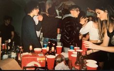 a group of people standing around a table filled with cups and drinks at a party