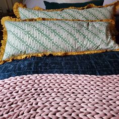 a bed with pink and green pillows on it's sides, next to a blue comforter