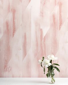 a vase with white flowers in front of a pink wallpapered background that looks like chevron lines