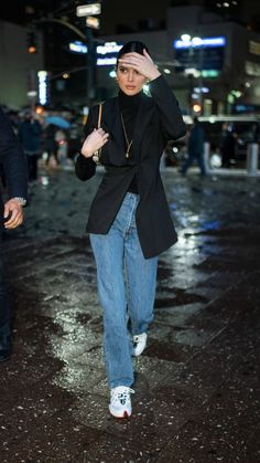 a woman in black jacket and jeans walking on street at night with umbrella up to her head