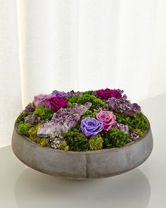 a bowl filled with flowers and moss on top of a white table next to a curtain