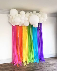 balloons and streamers are hanging from the ceiling in front of a rainbow colored wall