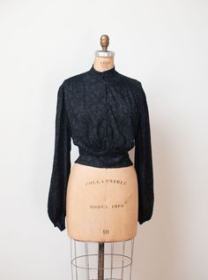 "Antique embroidered black blouse c. 1900 with gathering at the shoulders, long bishop sleeves with self fabric buttons at the cuffs and self fabric ties at the back. Metal snaps at the front. Feels like silk or a silk blend. - Size Small / Medium / Large - Blousy style tie to fit. Displayed unclipped on dress form with 35\" bust. Shoulder: 16\" Bust: 44\" - 46\" Waist: 42\" Length: 18.5\" Sleeve Length: 26\" Condition: Excellent! - One small hole as pictured. Only seen when held up to light. -