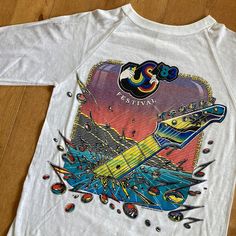 "This piece is a super cool vintage baseball style tee from the 1983 US Festival, a music festival held in San Bernardino, California in the early 1980s. This white tee has super colourful graphics on either side with an amazing one on the front of the neck of an electric guitar rising out of the ocean. On the back, the amazing performers for the show are listed including Willie Nelson, Alabama, Waylon Jennings and Hank Williams Jr. to name a few.  -50% Cotton, 50% Polyester -Single Stitch -No M Graphic Design Tops For Music Festival, Retro Festival T-shirt With Screen Print, Retro Printed Tops For Music Festivals, Retro Crew Neck T-shirt For Music Festival, Retro Tops For Concerts And Music Festivals, Retro Graphic Tops For Music Festivals, Vintage Graphic Design T-shirt For Music Festivals, Retro White T-shirt For Music Festival, Summer Band Merch Long Sleeve T-shirt