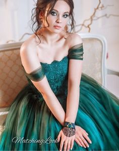 a woman in a green dress sitting on a chair with her hands on her knees