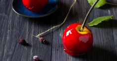 two red apples sitting on top of a wooden table next to leaves and fruit bowl