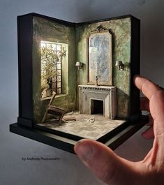 a hand is holding an open book with a painting on it and a fireplace in the corner