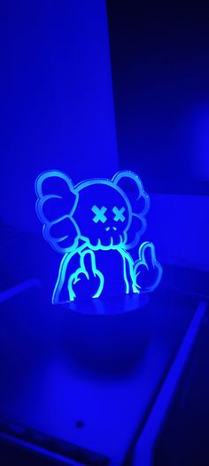 a lit up blue teddy bear sitting on top of a bowl in the dark with it's eyes closed