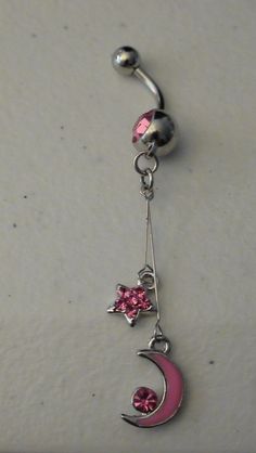 a pink and silver belly ring with stars, moon and heart dangling from it's side