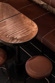 three stools and a table in front of a brown wall with tiles on it