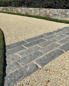 a stone walkway in front of a rock wall and green grass on the other side