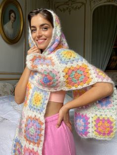 a woman wearing a colorful crochet shawl and smiling at the camera with her hands on her hips