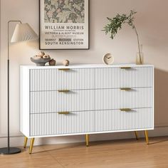 a white and gold dresser in a room with a plant on the side table next to it