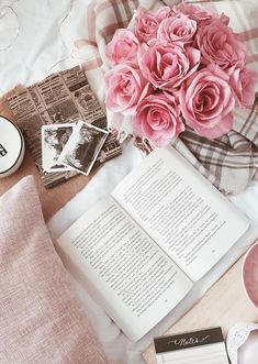 pink roses and coffee are on the bed next to an open book, tea cup, and photos